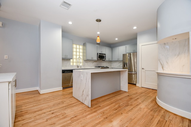 kitchen featuring stainless steel appliances, decorative light fixtures, light hardwood / wood-style flooring, a center island, and gray cabinets