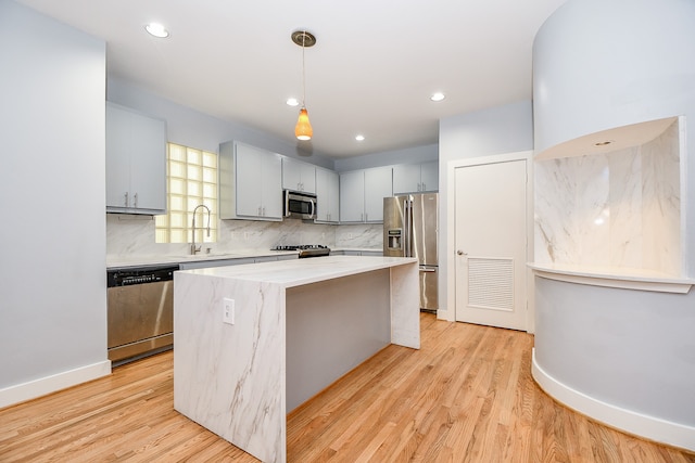 kitchen featuring sink, a center island, light hardwood / wood-style flooring, decorative light fixtures, and appliances with stainless steel finishes