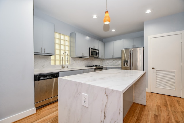 kitchen featuring sink, light hardwood / wood-style floors, decorative light fixtures, a kitchen island, and stainless steel appliances