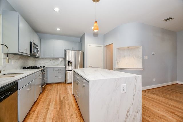 kitchen featuring decorative backsplash, stainless steel appliances, decorative light fixtures, light hardwood / wood-style flooring, and a kitchen island