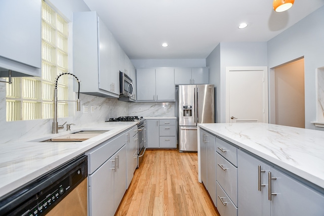 kitchen with sink, a healthy amount of sunlight, stainless steel appliances, light hardwood / wood-style flooring, and gray cabinets