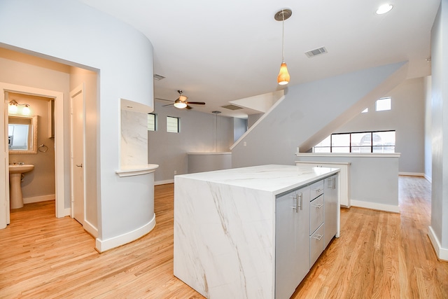 kitchen with ceiling fan, a center island, light stone counters, decorative light fixtures, and light wood-type flooring