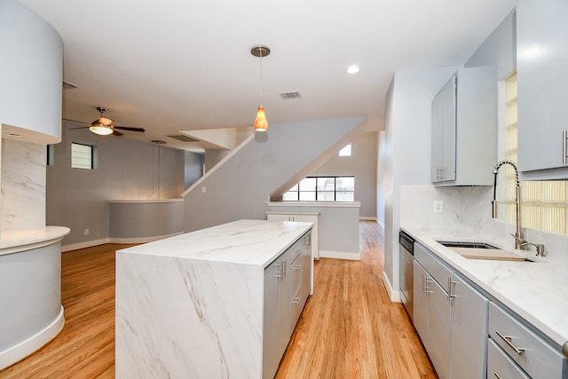 kitchen with sink, hanging light fixtures, stainless steel dishwasher, light hardwood / wood-style floors, and a kitchen island