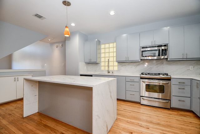 kitchen with hanging light fixtures, a kitchen island, stainless steel appliances, and light hardwood / wood-style flooring