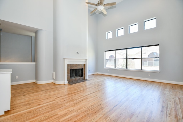 unfurnished living room featuring a tile fireplace, a towering ceiling, light hardwood / wood-style flooring, and ceiling fan