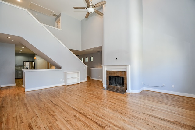 unfurnished living room featuring a tile fireplace, ceiling fan, light hardwood / wood-style flooring, and a towering ceiling