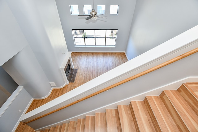 stairs with a fireplace, ceiling fan, hardwood / wood-style floors, and a towering ceiling