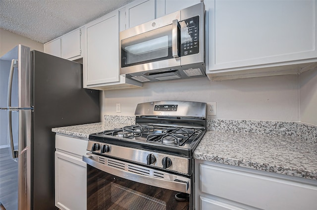 kitchen featuring white cabinets, a textured ceiling, stainless steel appliances, and light stone countertops