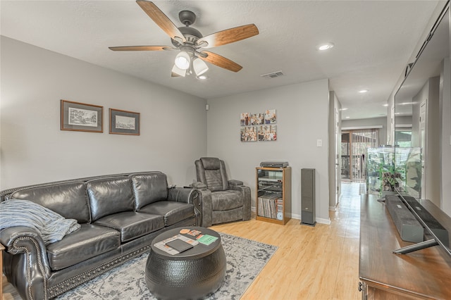 living room featuring ceiling fan, light wood-type flooring, and a textured ceiling