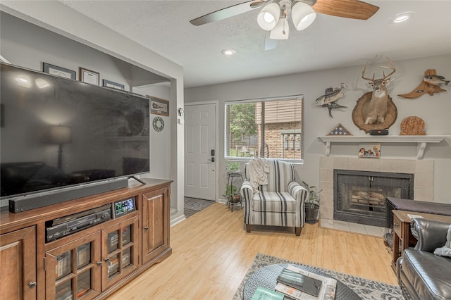 living room featuring a tile fireplace, a textured ceiling, light hardwood / wood-style floors, and ceiling fan