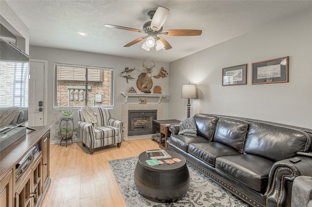 living room with a fireplace, a textured ceiling, light hardwood / wood-style floors, and ceiling fan