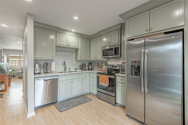 kitchen with light stone countertops, appliances with stainless steel finishes, light wood-type flooring, backsplash, and sink