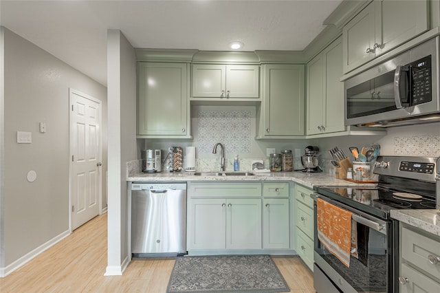 kitchen with light stone countertops, sink, stainless steel appliances, backsplash, and light hardwood / wood-style floors