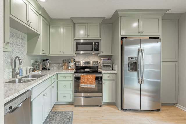 kitchen with light stone countertops, sink, stainless steel appliances, tasteful backsplash, and light hardwood / wood-style flooring