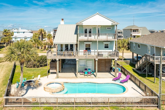 back of property with a swimming pool with hot tub, a patio, a balcony, and an outdoor fire pit