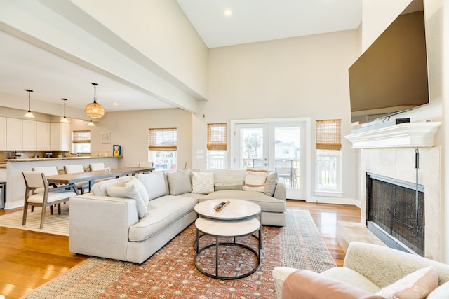 living room featuring light wood-type flooring, a fireplace, a wealth of natural light, and a high ceiling