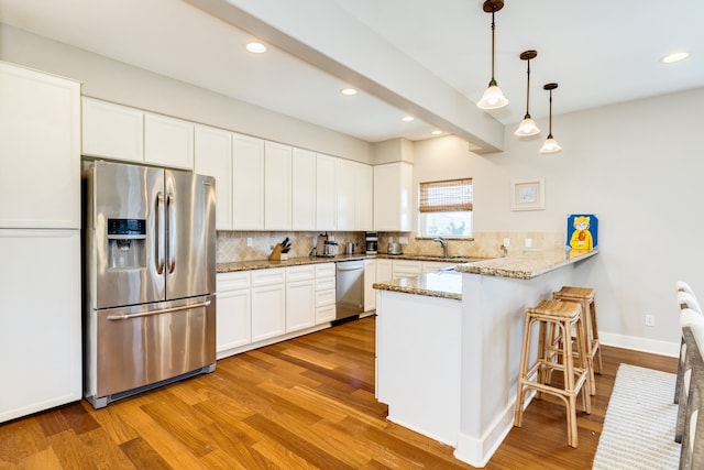 kitchen featuring pendant lighting, kitchen peninsula, light wood-type flooring, appliances with stainless steel finishes, and white cabinetry