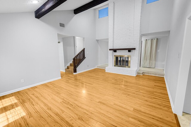 unfurnished living room with high vaulted ceiling, beam ceiling, light hardwood / wood-style floors, and a brick fireplace