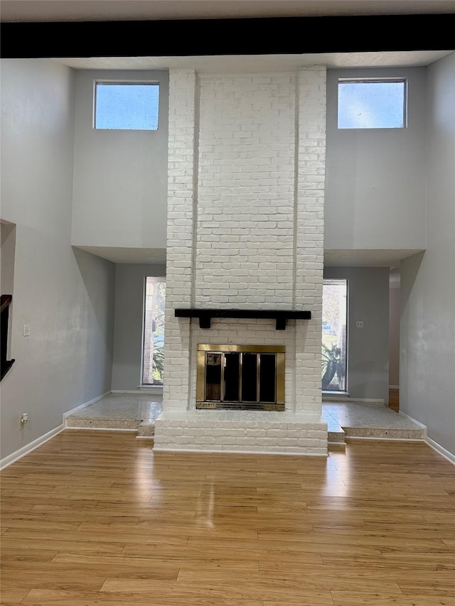 unfurnished living room with a high ceiling, a brick fireplace, light hardwood / wood-style floors, and plenty of natural light