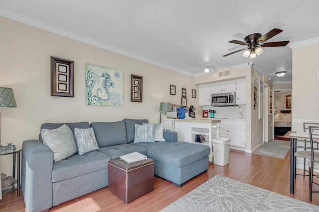 living room with ceiling fan, ornamental molding, and light wood-type flooring