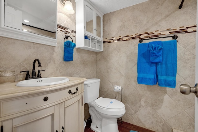 bathroom with a textured ceiling, vanity, tile walls, and toilet