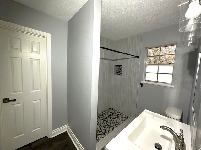 bathroom featuring sink, a textured ceiling, toilet, tiled shower, and hardwood / wood-style flooring