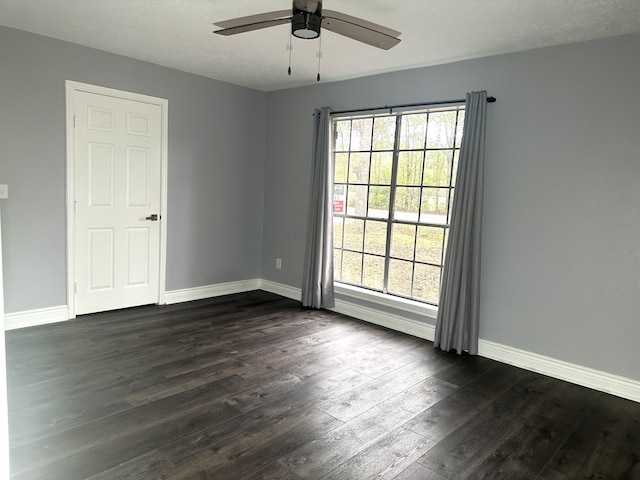 spare room featuring plenty of natural light, ceiling fan, and dark wood-type flooring