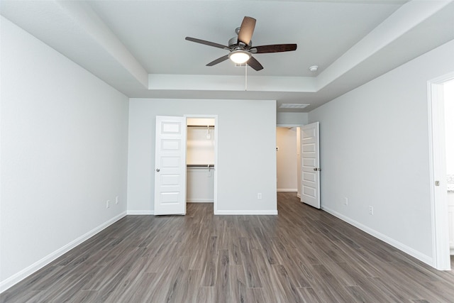 unfurnished bedroom featuring ceiling fan, a raised ceiling, a spacious closet, and a closet