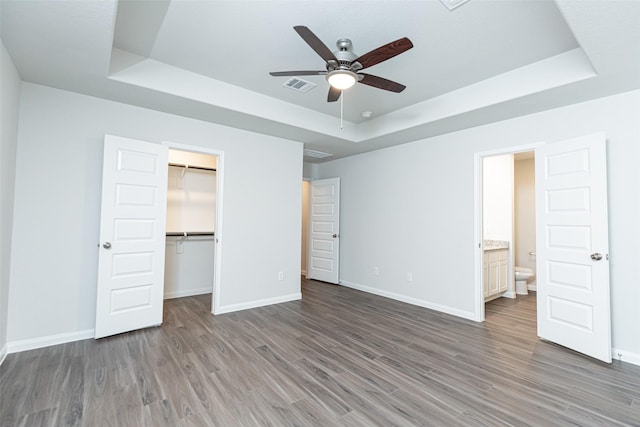 unfurnished bedroom featuring a tray ceiling, ceiling fan, ensuite bathroom, and a spacious closet