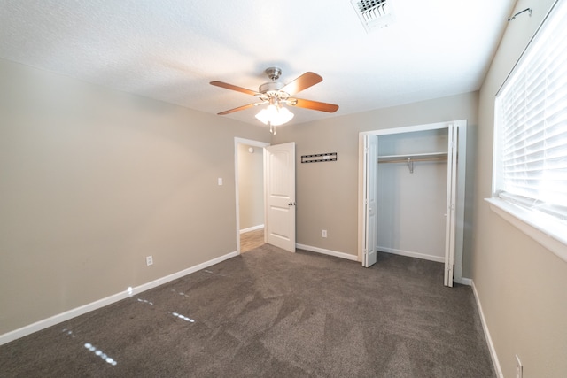 unfurnished bedroom with ceiling fan, dark carpet, and a closet