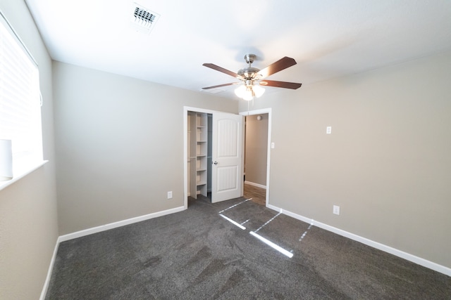 unfurnished bedroom featuring a walk in closet, a closet, dark carpet, and ceiling fan