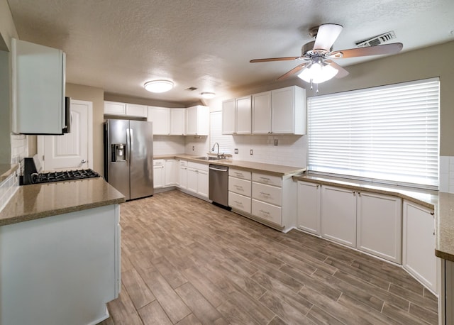 kitchen with light stone counters, stainless steel appliances, sink, light hardwood / wood-style floors, and white cabinetry