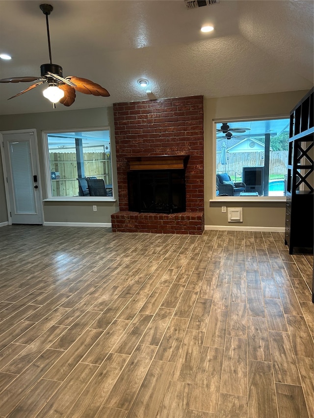 unfurnished living room with ceiling fan, wood-type flooring, a textured ceiling, and a brick fireplace