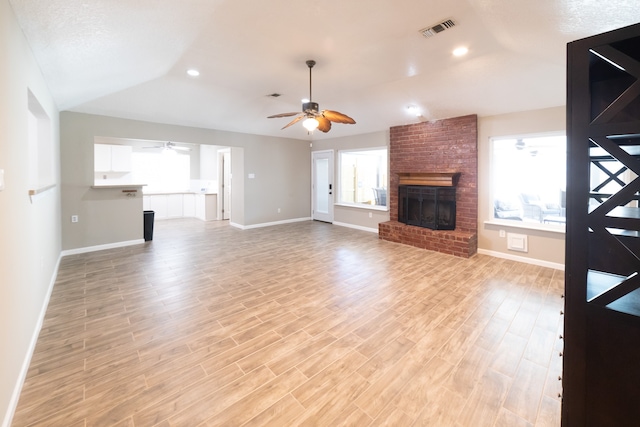 unfurnished living room featuring light hardwood / wood-style flooring, a healthy amount of sunlight, vaulted ceiling, and a brick fireplace