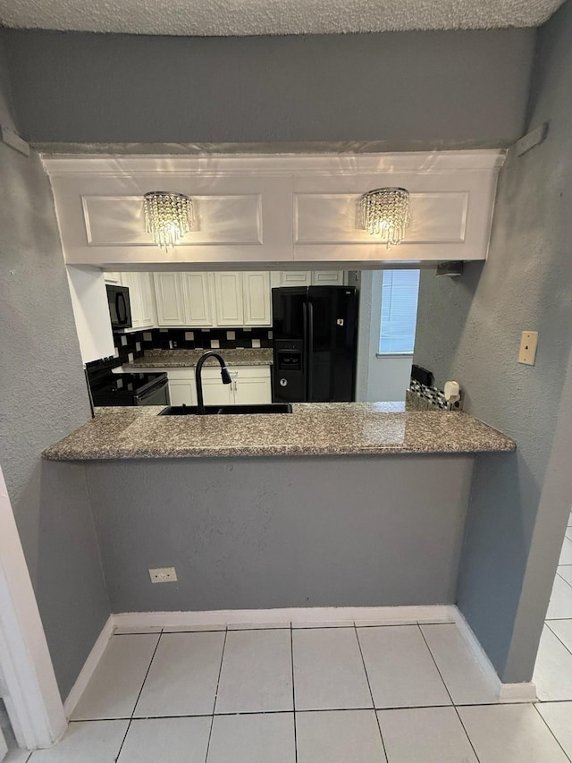 kitchen with sink, black appliances, light tile patterned floors, stone countertops, and white cabinetry