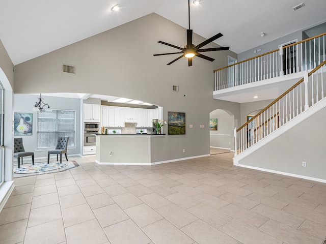 unfurnished living room featuring light tile patterned floors, high vaulted ceiling, and ceiling fan with notable chandelier