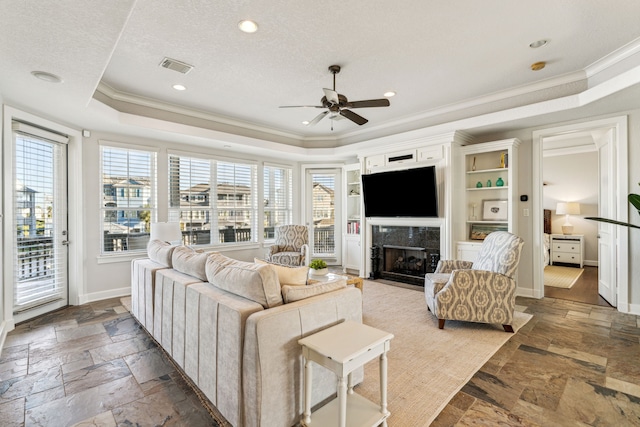 living room featuring a fireplace, a tray ceiling, ceiling fan, and crown molding