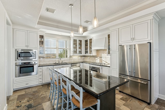 kitchen with custom exhaust hood, dark stone counters, appliances with stainless steel finishes, a kitchen island, and a breakfast bar area