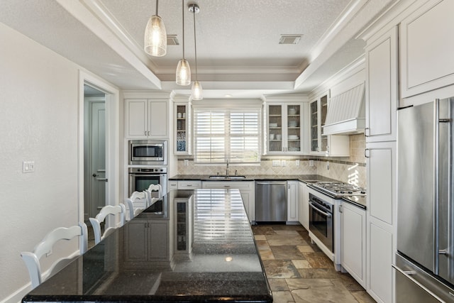 kitchen featuring white cabinetry, stainless steel appliances, pendant lighting, a tray ceiling, and custom exhaust hood