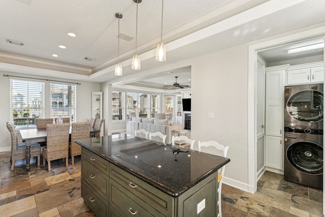 kitchen featuring a raised ceiling, white cabinetry, a wealth of natural light, and stacked washer and clothes dryer