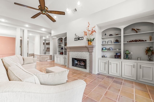 living room featuring built in shelves, ceiling fan, a fireplace, and vaulted ceiling