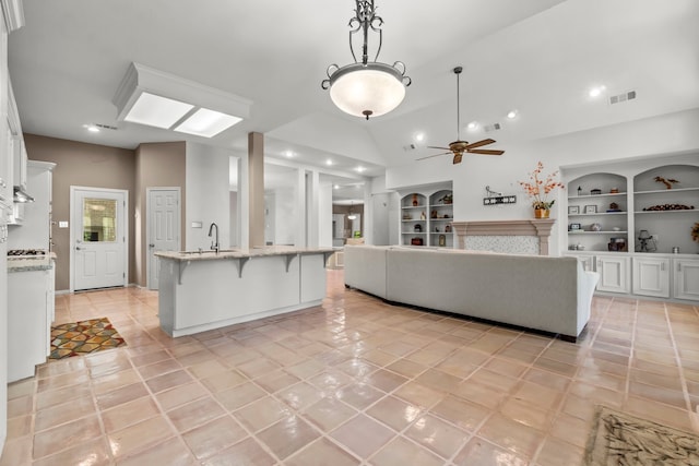 tiled living room featuring built in shelves, ceiling fan, lofted ceiling, and sink