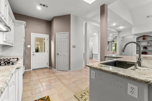 kitchen with white cabinets, stainless steel gas stovetop, light stone countertops, and sink