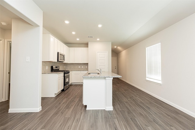 kitchen with light stone countertops, sink, stainless steel appliances, a kitchen island with sink, and white cabinets