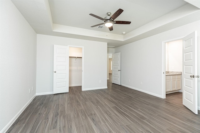 unfurnished bedroom with a walk in closet, ceiling fan, a tray ceiling, dark hardwood / wood-style flooring, and a closet