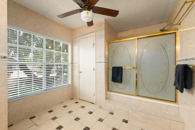 bathroom with ceiling fan, a shower with door, a textured ceiling, and tile walls