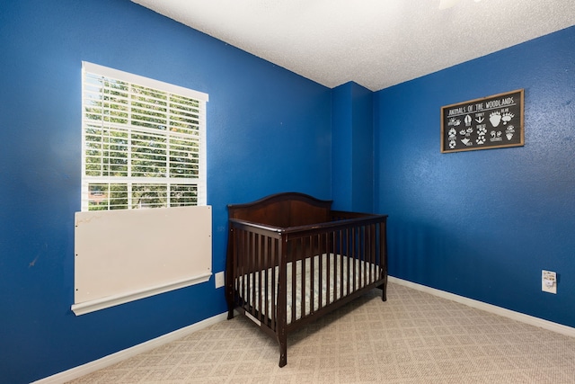 bedroom with a crib, a textured ceiling, and carpet flooring