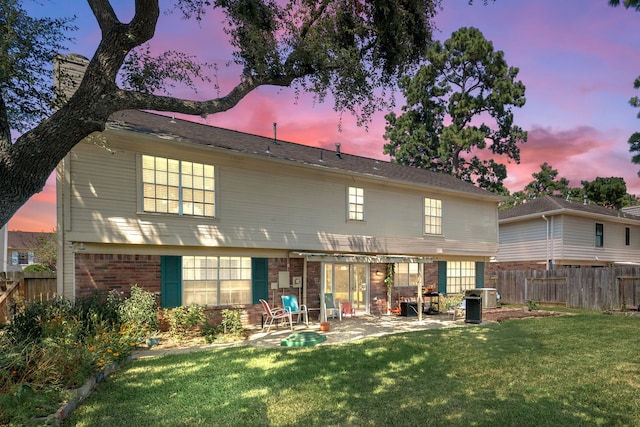 back house at dusk featuring a lawn and a patio area