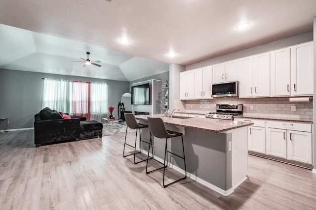 kitchen featuring light stone counters, stainless steel appliances, white cabinetry, lofted ceiling, and an island with sink