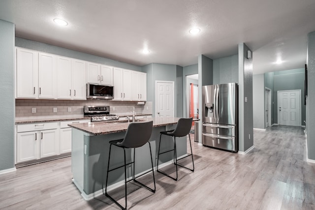 kitchen featuring dark stone counters, white cabinets, an island with sink, and stainless steel appliances